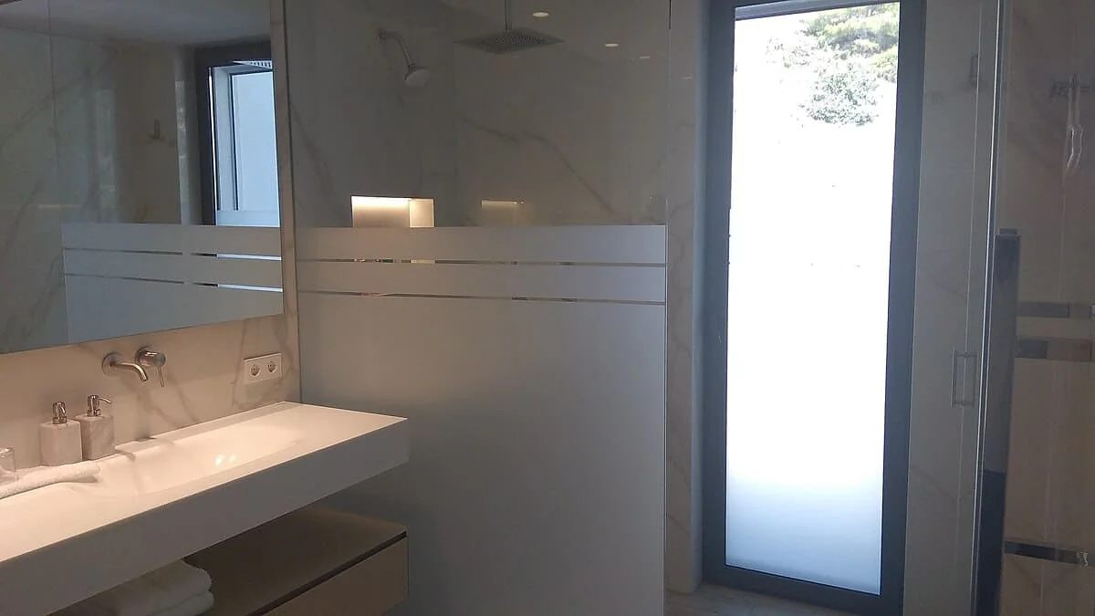 Banded decorative window film and frosted door panel in a marble bathroom